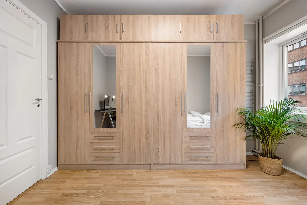 Clóset empotrado de madera clara con puertas de espejo y gavetas en una habitación.